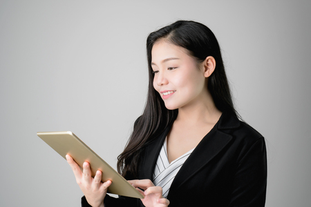 Smiling business women are holding tablet and using online applications. Gray background provides soft lighting.の写真素材