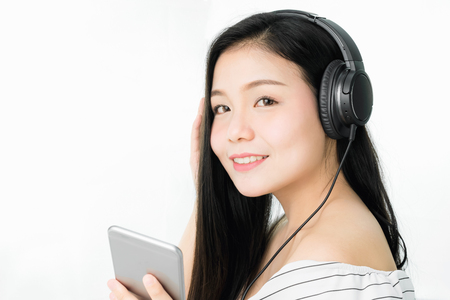 Asian Women are listening to music from black headphones. In a comfortable and good mood, on a white background gives a soft light.の写真素材