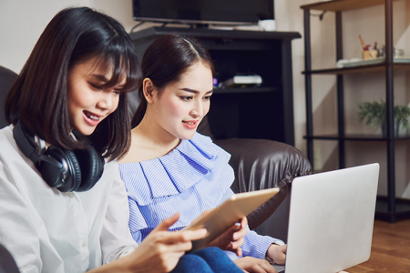 Asian girl in blue casual dress listening to music from black headphones and use laptop. In a comfortable and good mood, In the living room on the sofa.の写真素材