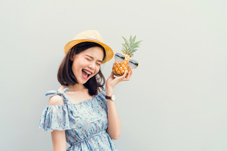 Young girl happy smile and cheerful in blue dress, hold two pineapple in hand. Concept summer travel.の写真素材