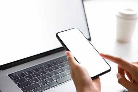 Woman holding smartphone mockup of blank screen and laptop on the table.の写真素材