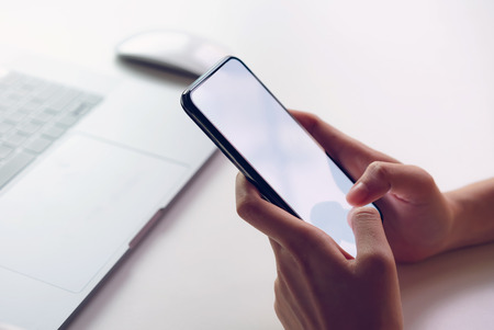 Woman holding smartphone mockup of blank screen on the table.