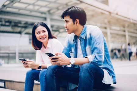Young people are using smartphone and smiling while sitting on free time. technology conceptの写真素材