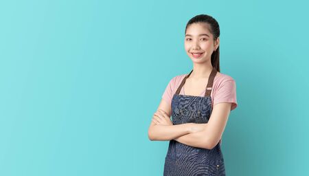 Small business, Asian woman in apron and standing with crossed arms against and looking forward on blue background.の写真素材