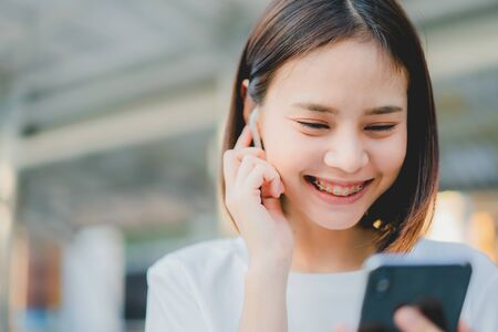 Asian women of happy smiling are listening to music from white headphones. And using hands touch to...