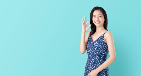 Portrait smile happily Asian woman shows ok sign and looking at the camera over blue background, Cheerful girl gestures studio.の写真素材