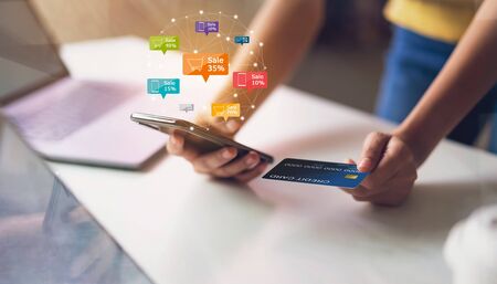Woman holding smartphone with icon discount label and cart online, credit card on the table....