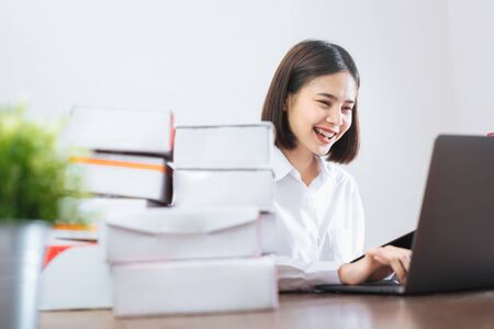 Happy smiling Asian woman using laptop computer checking order for customer and online delivery for ready packaging.の写真素材