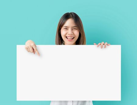 Young Asian woman holding blank paper with smiling face and looking on the blue background. for advertising signs.の写真素材
