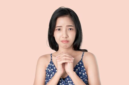 Portrait of young Asian woman frowns face is going to cry and hands clasped and has some request on light background.の写真素材