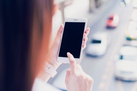 Woman hand using white smartphone and background of car on the road.の写真素材