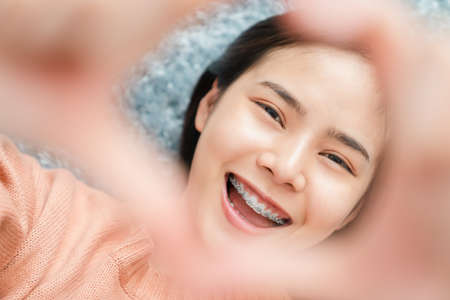Cheerful beautiful Asian woman in a orange shirt lying on floor and hand touching camera at house.の写真素材