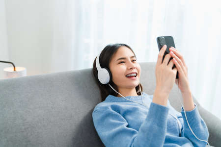 Asian woman of happy smiling are listening to music from white headphones and using hands touch...