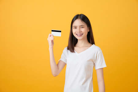 Attractive smiling Asian woman holding credit card payment on yellow background with copy space.の写真素材