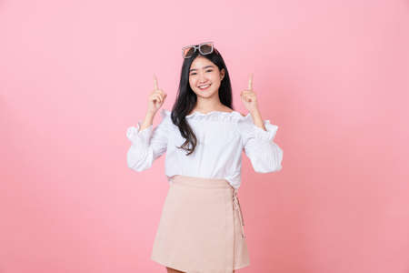 Smiling Asian woman stand and pointing finger on pink background.の写真素材