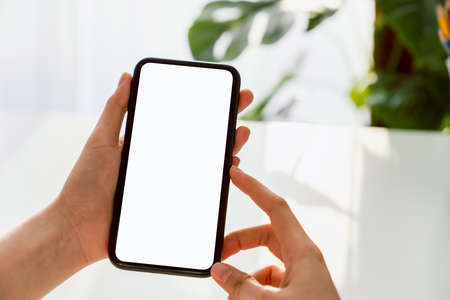 Hand holding smartphone mockup of blank screen on the table. Take your screen to put on advertising.の写真素材