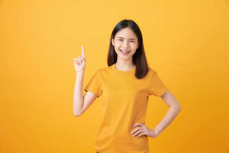 Smiling Asian woman stand and pointing finger on orange background.の写真素材