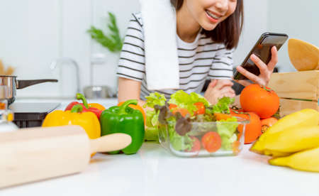 Woman hand holding a smartphone and salad bowl with tomato and various green leafy vegetables on the table at the home, take your advertising.の写真素材