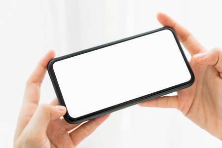 Hand holding smartphone mockup of blank screen on the table. Take your screen to put on advertising.の写真素材