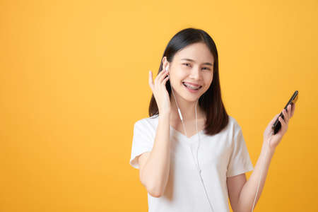 Happy Asian woman holding smartphone and listening to music on pink background.の写真素材