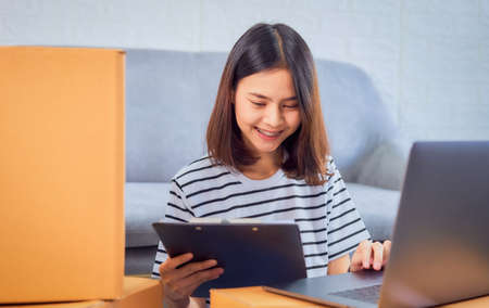 Smiling Asian woman owner check the customer order from the computer, seller prepares the delivery box. Startup small business concept.の写真素材