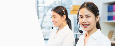 Smiling Asian businesswoman consultant wearing microphone headset of customer support phone operator at workplace.の写真素材