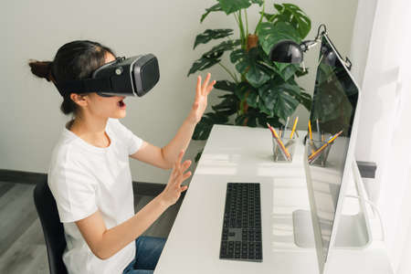 Excited young Asian woman using a virtual reality headset and joysticks, Concept connection and...