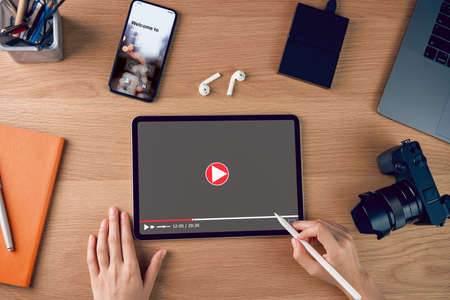 Woman using digital tablet and watching video online with camera and accessories on wood table.の写真素材