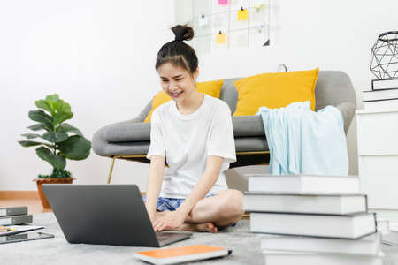 Happy young Asian woman working for laptop with graph documents from home on the carpet, meeting and training online concept.の写真素材