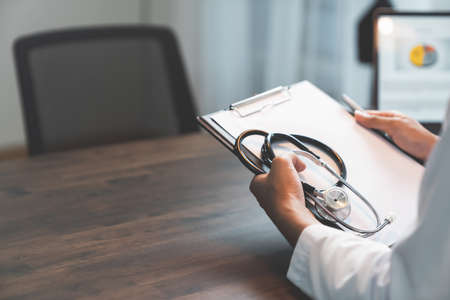 Close up of doctor sitting hands holding stethoscope with chart report at the table, Healthcare and medical.の写真素材