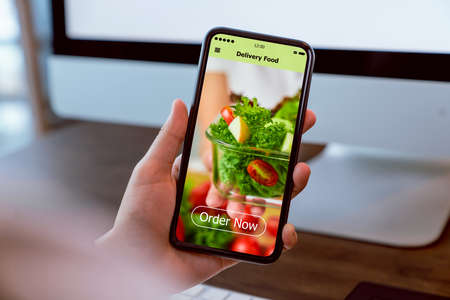 Woman using smartphone and touching application screen for ordering salad online on the table at office.の写真素材