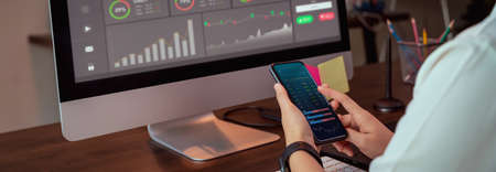 Stock exchange market concept, businesswoman trader looking on smartphone and computer with graphs analysis candle line on table in office, diagrams on screen. proportion of the banner for ads.の写真素材
