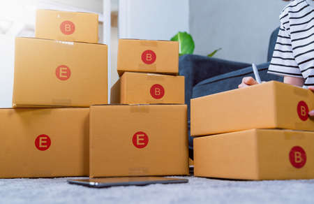Startup small business concept, young woman owner working and packing on the box to customer at the sofa in home office, seller prepares the delivery.の写真素材