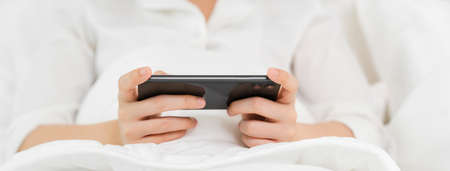 Woman just woke up in the morning and on the bed picking up the phone to check on her social media.の写真素材