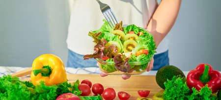 Close-up of woman hands showing salad bowl and various green leafy vegetables on the table at the home.の写真素材