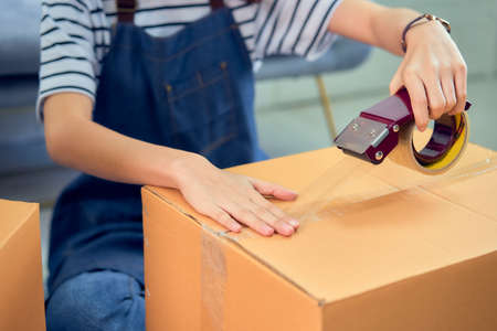 Startup small business concept, young Asian woman owner working and packing on the box to customer at the sofa in home office, seller prepares the delivery.の写真素材