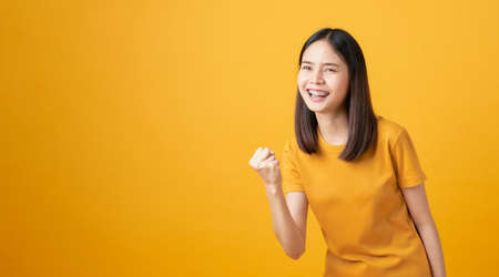 Young smiling Asian woman stand with amazed for success and looking to copy space on yellow...