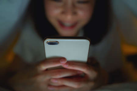 Close-up of woman holding a smartphone and using online social on the bed at night. Technology for communication concept.の写真素材