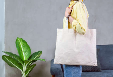 Woman in casual yellow t-shirt stand and holding bag canvas fabric for mockup logo.の写真素材