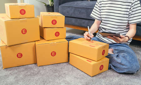 Startup small business concept, young woman owner working and packing on the box to customer at the sofa in home office, seller prepares the delivery.の写真素材