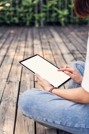 Woman hand sitting and holding digital tablet with blank screen on the park.の写真素材