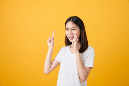 Attractive young asian woman announcing with hands to the mouth  and telling a secret, isolated on light orange backgroundの写真素材