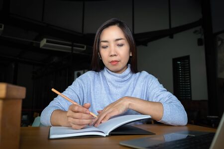 A smart beautiful clever Asian female write and note down information of summary positive study and business script essay on notebook in her modern office table with the comfort atmosphereの写真素材