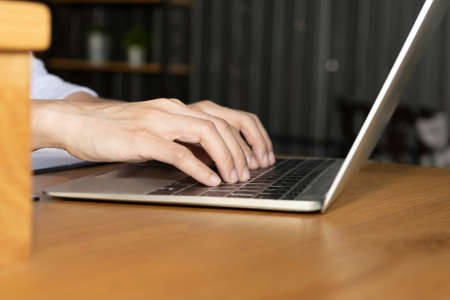 Side view and close up of young woman hands are typing on the modern laptop computer keyboard on wooden office table desktop with supplies for business and technology concept.の写真素材