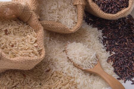 Three kinds of rice in small burlap bags and spoon on white background