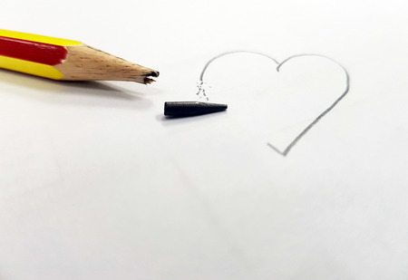 Sharpened pencil over a blank old sheet of paper with a broken tip,Drawing a heart not complete.の写真素材