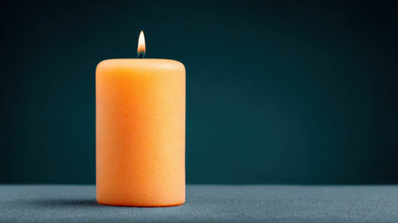 A lit candle sits on a table. The candle is orange and has a small flame. Concept of warmth and comfort, as the candle's light illuminates the surrounding areaの素材