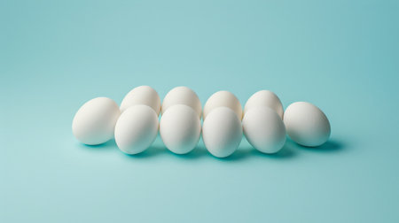 A dozen white eggs arranged in a row on a blue background.の素材