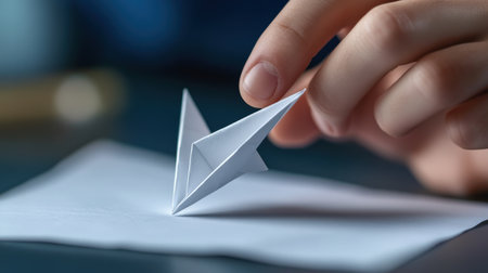 A close-up of fingers showing how to fold a paper airplane.の素材