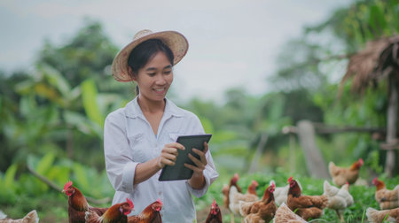 Smiling Asian female farmer using a tablet to monitor the health of her free range chickens on an organic farmの素材